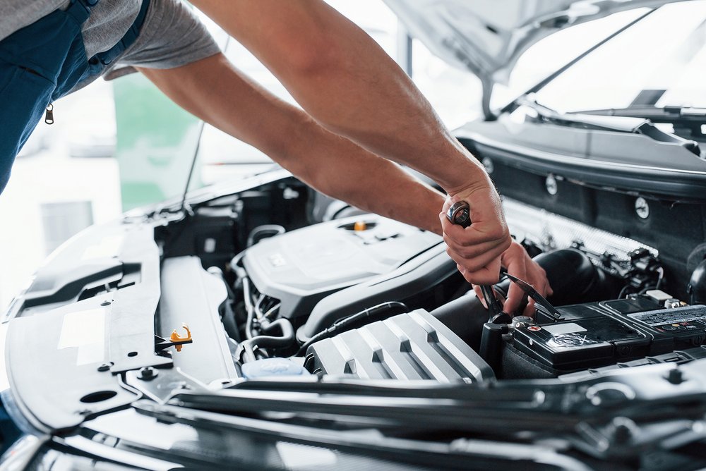 Kfz-Mechaniker arbeitet mit Werkzeug am offenen Motorraum eines Autos.