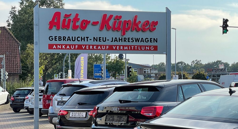 Ein Autohaus-Schild mit der Aufschrift „Auto-Küpker“ über einem Parkplatz voller Fahrzeuge.