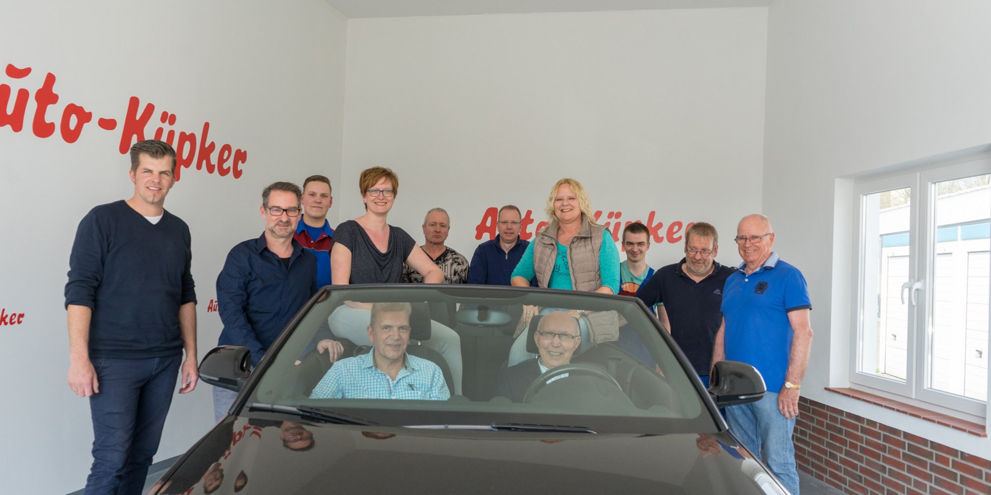 Das Bild zeigt ein Team von Mitarbeiterinnen und Mitarbeitern, die sich um ein Auto in einem Ausstellungsraum des Autohauses versammelt haben.
